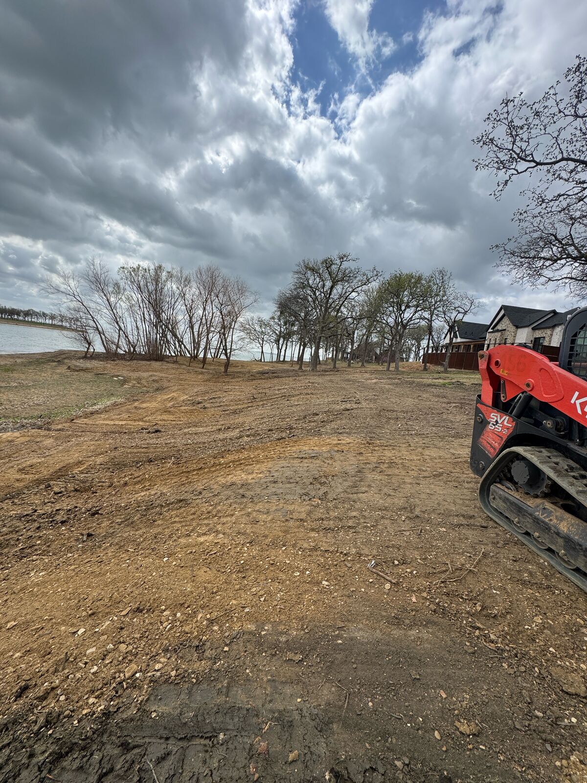 Freshly cleared and graded lot with a skid steer parked at the edge